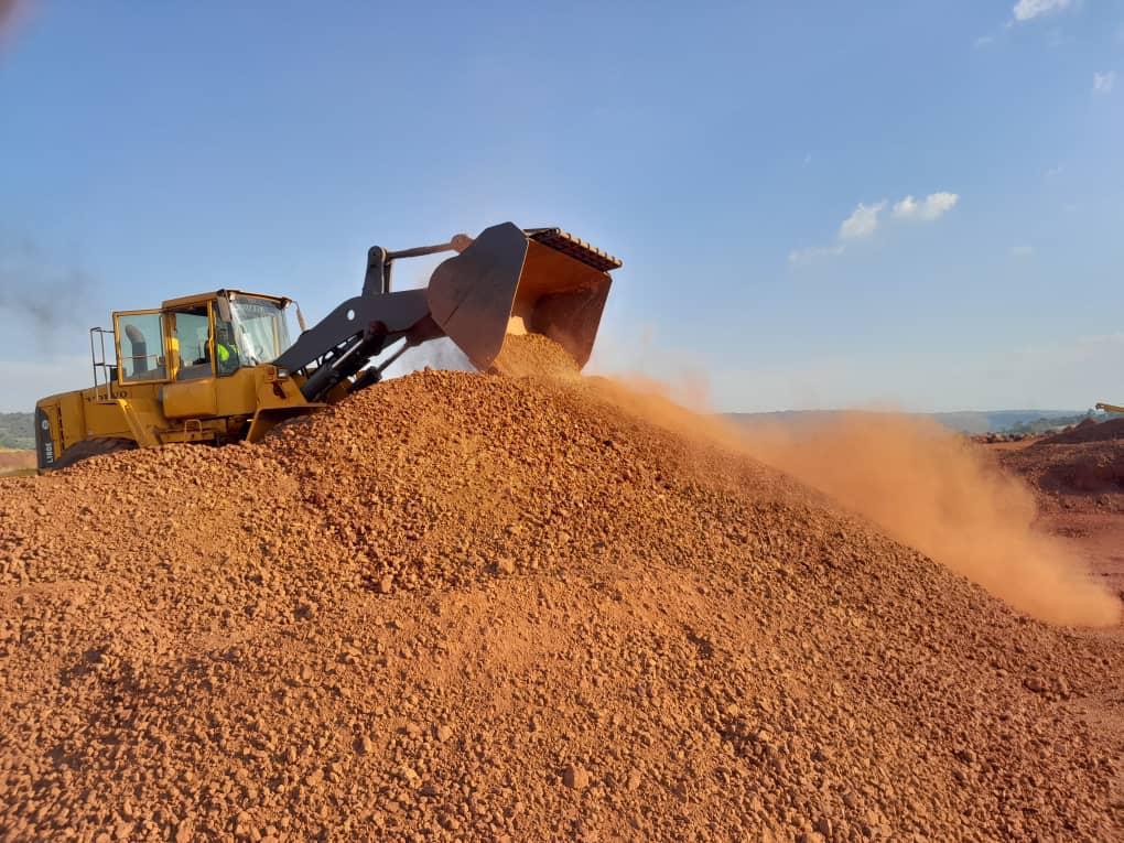 Bulldozer pushing a large pile of orange gravel under a clear sky.