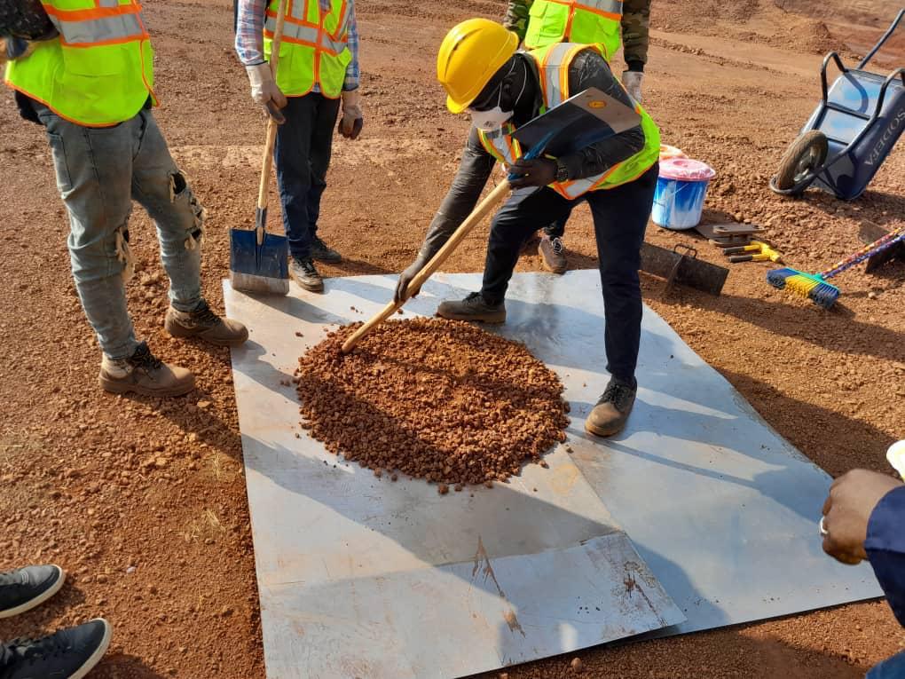Worker leveling a pile of soil on a metal sheet at a construction site.