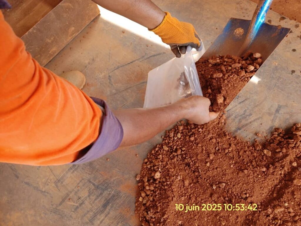 Person filling a bag with reddish soil or compost using a scoop.