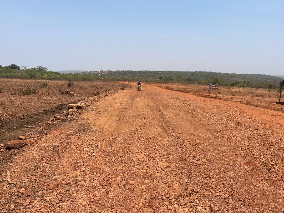 A wide, rough dirt road stretches through a barren, dry landscape under a clear sky.