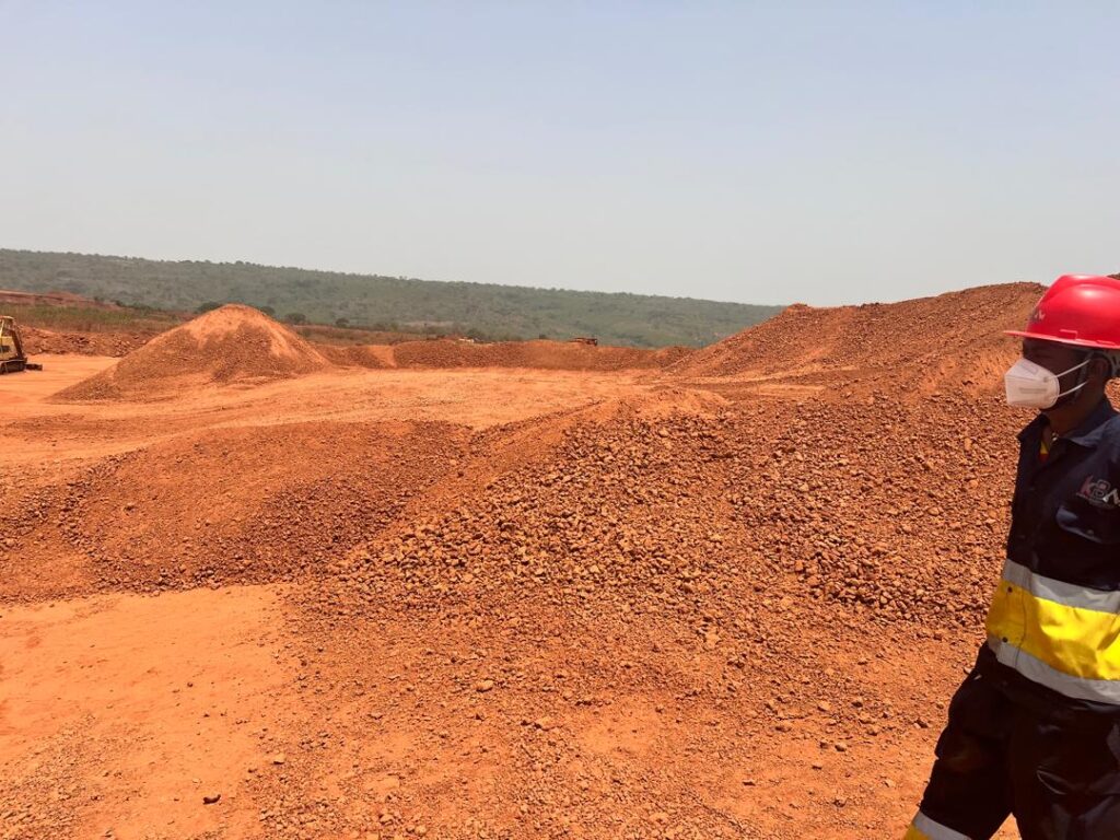Expansive landscape of reddish soil and gravel piles under a clear sky.