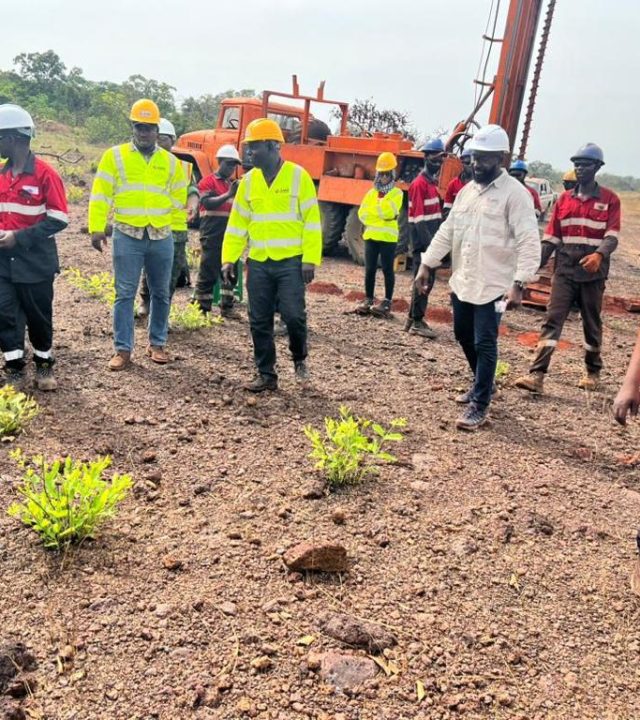 Group of people inspecting a construction site with machinery in the background.